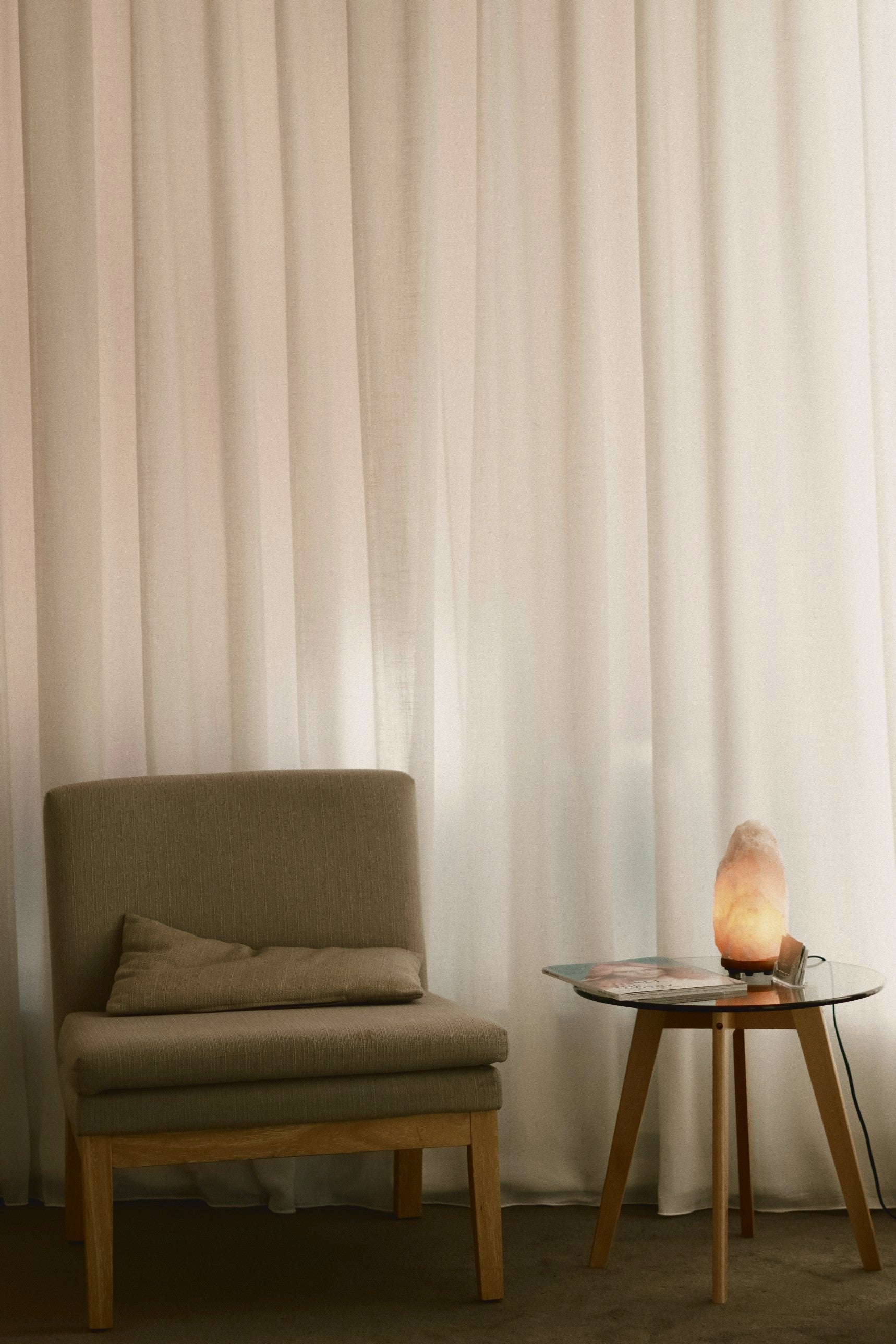 A calm consultation corner with a linen chair, sheer curtains and a glowing salt lamp