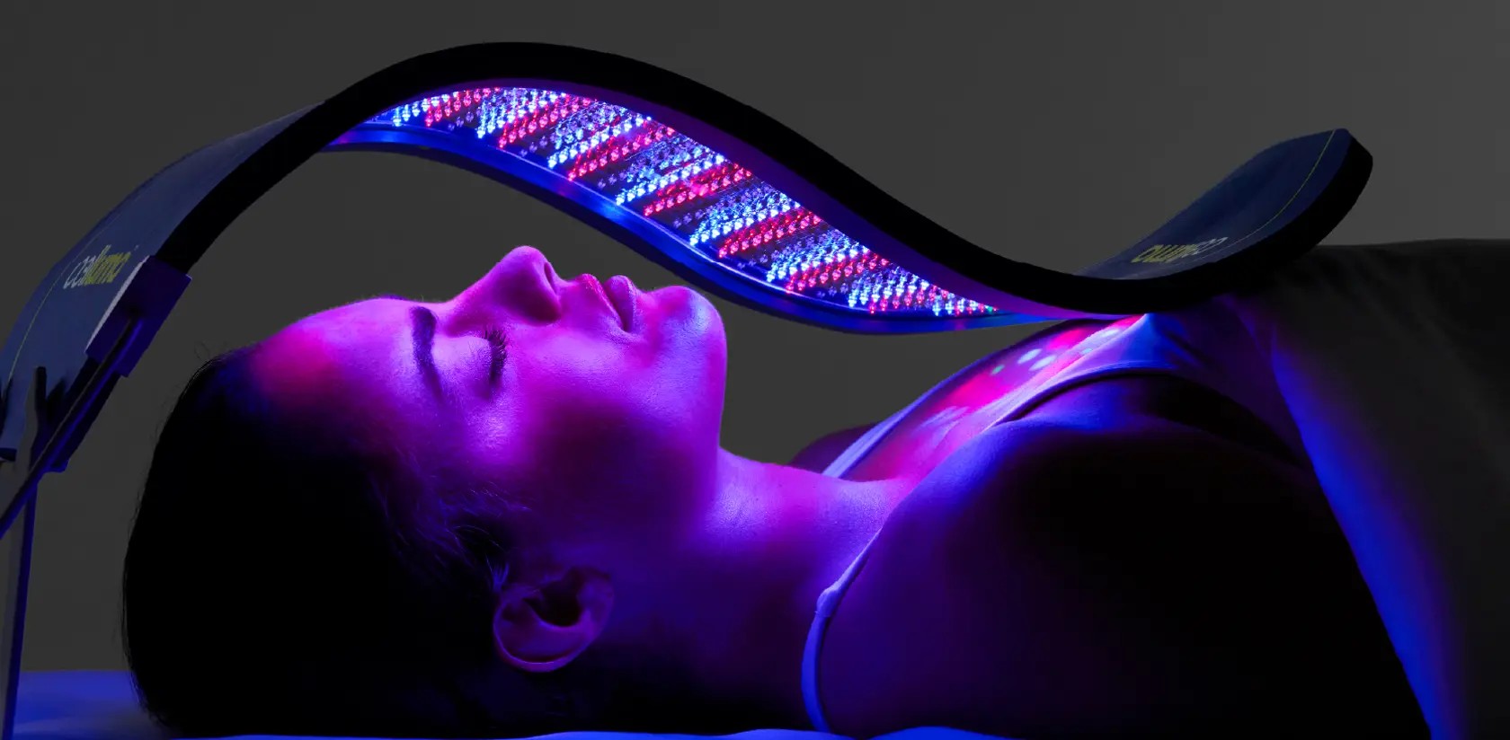 A client relaxing under a curved Celluma LED panel glowing red and blue